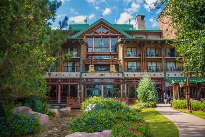 The front view of Disney's Wilderness Lodge with a walkway, creek, trees, and landscaping.